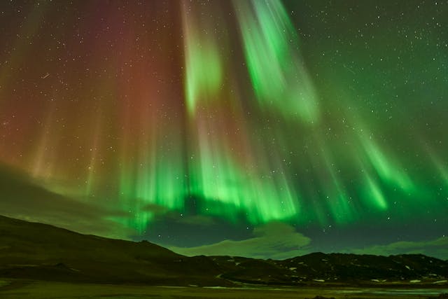 Auroras boreales verdes y rojas iluminando el cielo nocturno sobre un paisaje montañoso