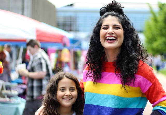 Familia disfrutando de un mercado callejero Mujer sonriente con su hija en un mercado al aire libre celebrando el Mes del Orgullo.