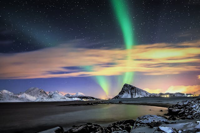 Auroras boreales sobre paisaje costero con montañas nevadas y cielo estrellado