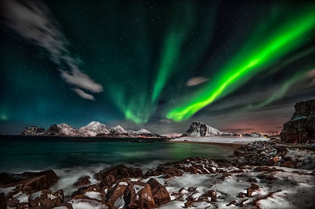 Auroras boreales sobre montañas nevadas y mar en paisaje nocturno