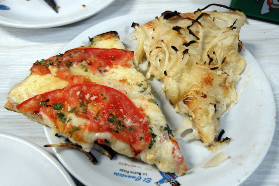 Dos porciones de pizza argentina al molde, una de muzzarella con tomate y otra de fugazza con cebolla