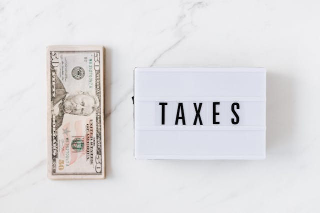 Impuestos y tasas en viajes internacionales Billete de 50 dólares junto a cartel con la palabra taxes sobre mármol blanco