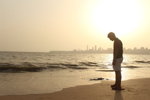 Atardecer en la playa de Mumbai, India Hombre contemplando el mar al atardecer en playa de Mumbai con ciudad al fondo