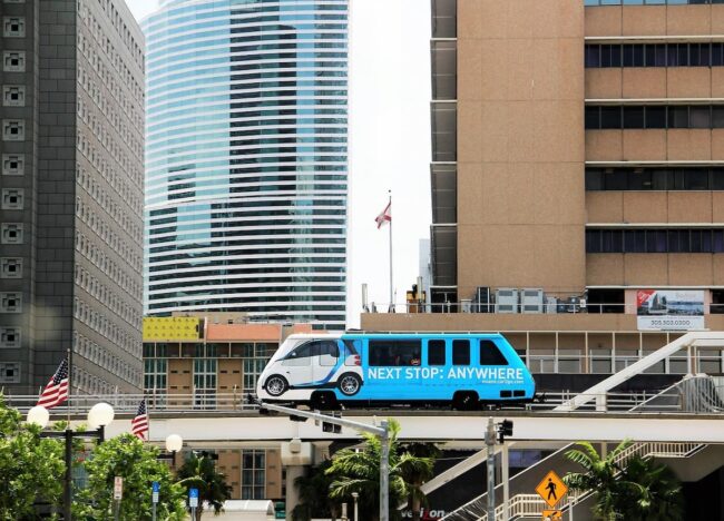 Transporte público en Miami: vehículo elevado sobre la ciudad Imagen de un vehículo de transporte público en una vía elevada de Miami, con rascacielos de fondo y el cartel "Next Stop: Anywhere". La escena muestra una mezcla de modernidad y urbanismo en la ciudad.