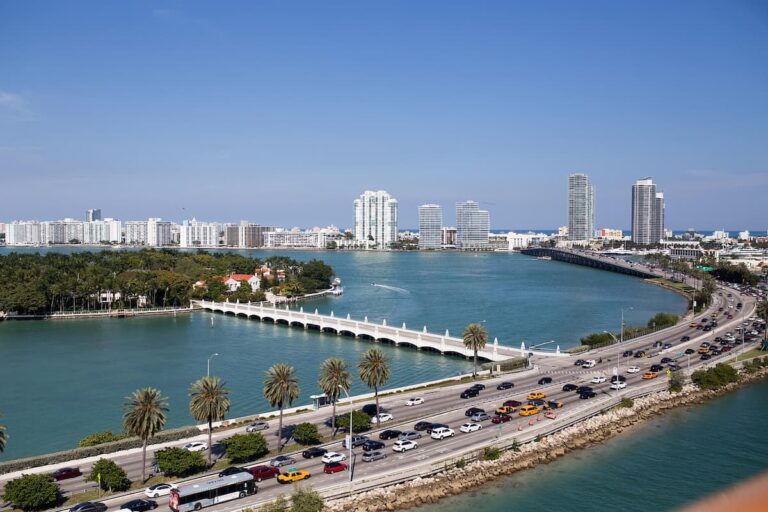 Vista aérea de Miami, mostrando un puente, la carretera y edificios altos a lo lejos. La imagen captura el contraste entre el agua y la ciudad.