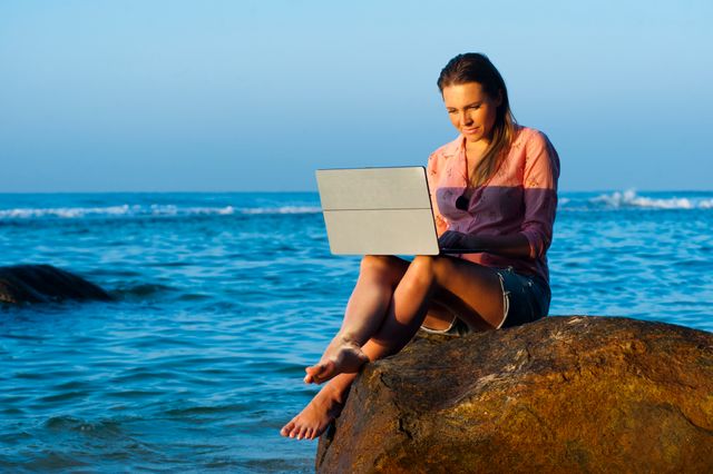 Mujer trabajando con una computadora frente al mar, imagen relacionada con una guía sobre qué es una Working Holiday Visa.