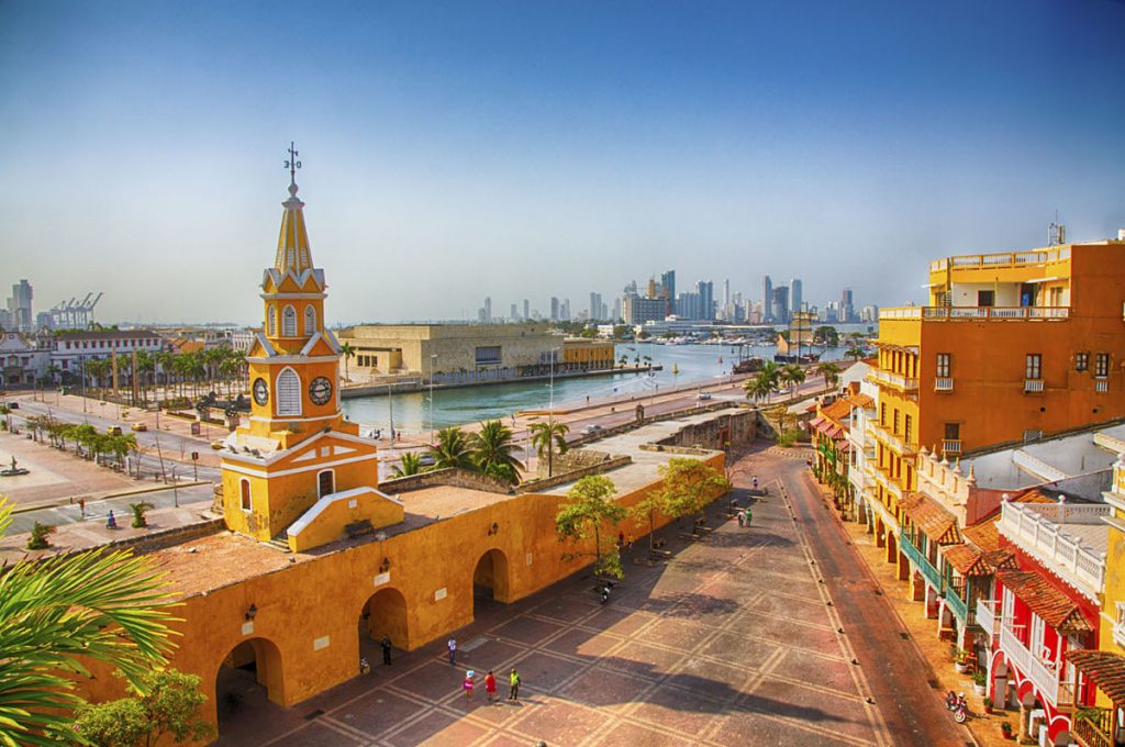 Vista panorámica del centro histórico de Cartagena de Indias con la Torre del Reloj, el puerto y los modernos edificios al fondo, en un día soleado.