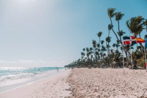 Playa de Punta Cana con palmeras, banderas y turistas caminando junto al mar