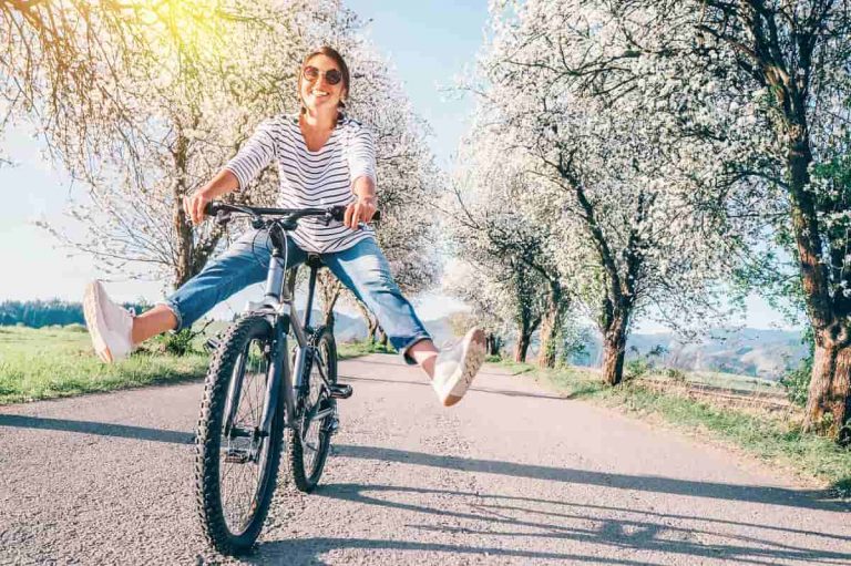 mujer en bicileta en un camino lleno de arboles en flor