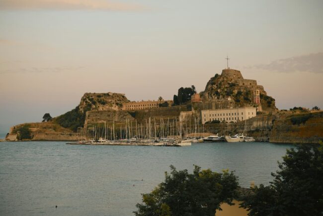 Vista de la Fortaleza Vieja de Corfú al atardecer, con barcos amarrados en el puerto.