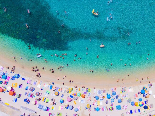 Playa de Corfú vista desde el aire Vista aérea de una playa en Corfú con sombrillas de colores y mar turquesa.