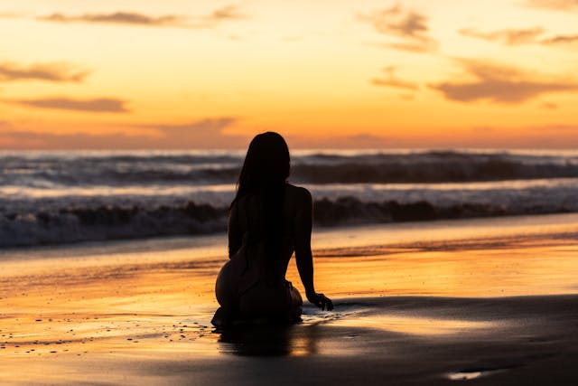 Persona sentada frente al mar al atardecer en una playa tranquila, ideal para experiencias relajadas en playas nudistas del mundo