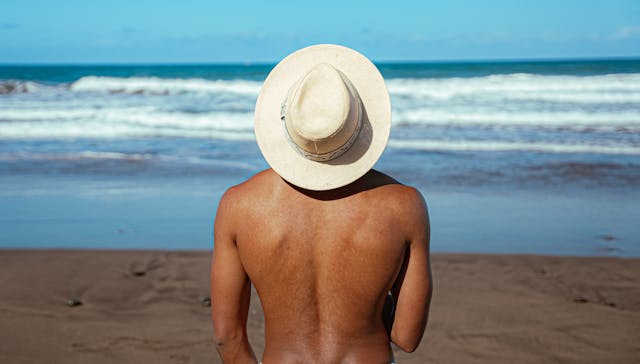 Persona de espaldas mirando el mar en una playa tranquila, escenario típico de playas nudistas en el mundo