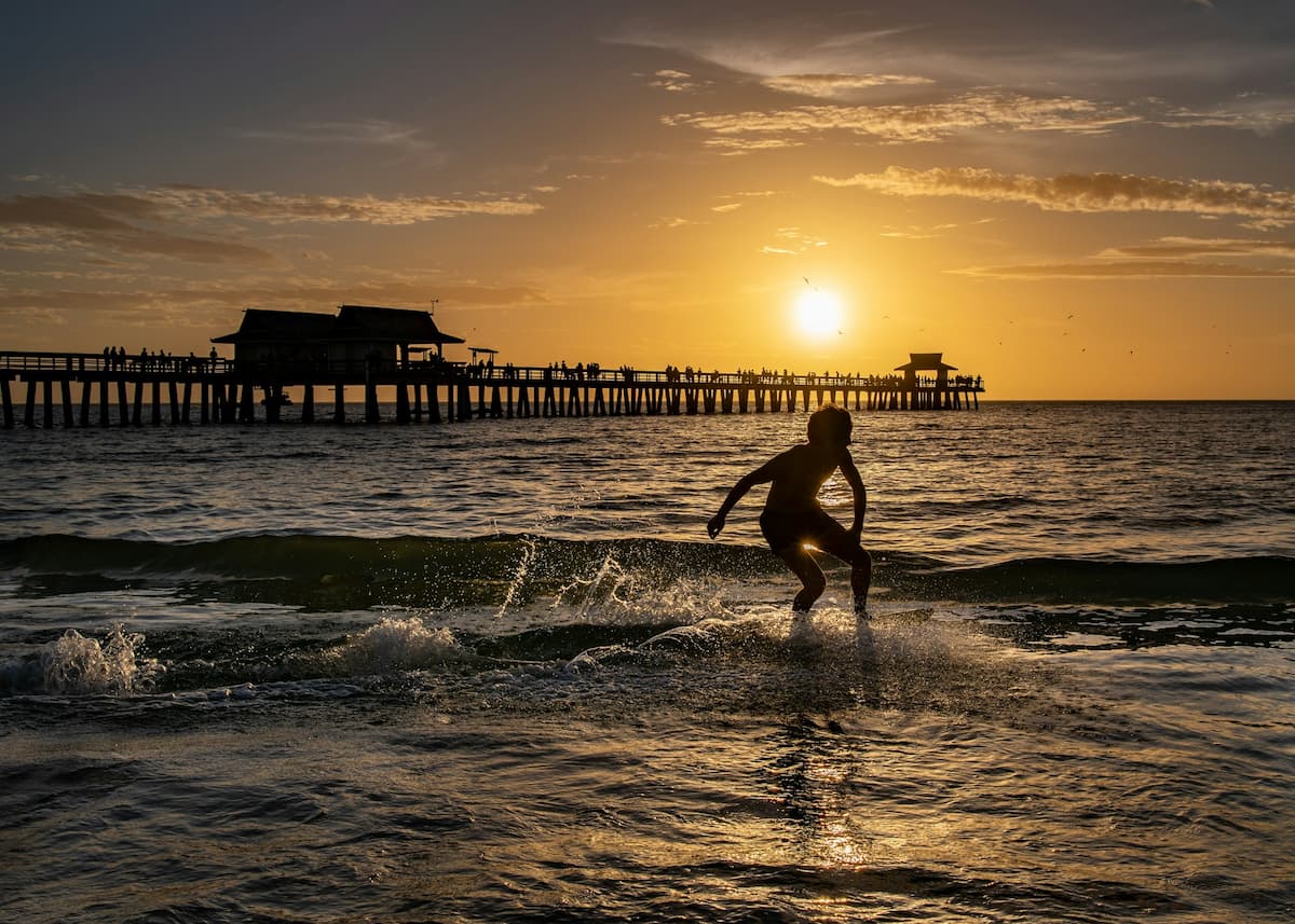 Surfista en el mar durante el atardecer en el muelle de Naples, Florida.