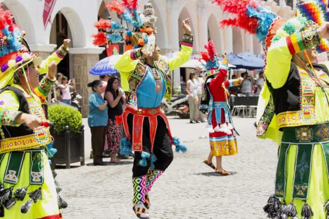 Bailarines con trajes típicos multicolores en celebración tradicional en plaza latinoamericana