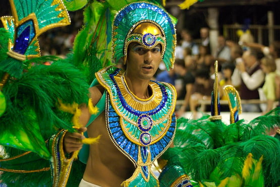 Hombre con traje colorido de plumas verdes y doradas en desfile de carnaval