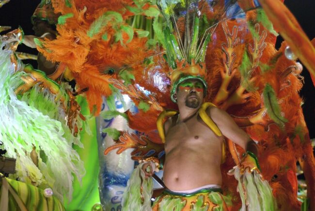 Traje colorido de carnaval en desfile latinoamericano Hombre con traje de carnaval en colores naranja y verde desfilando en fiesta popular