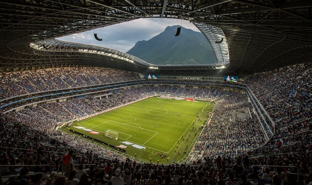 Interior de un estadio de fútbol en Monterrey con el Cerro de la Silla al fondo, una imagen que muestra la combinación de deporte, ciudad y paisaje montañoso que caracteriza a la capital de Nuevo León.