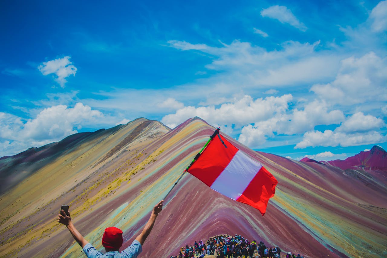 Turista con la bandera de Perú en la cima de la Montaña de 7 Colores, uno de los destinos más impresionantes de Cusco.
