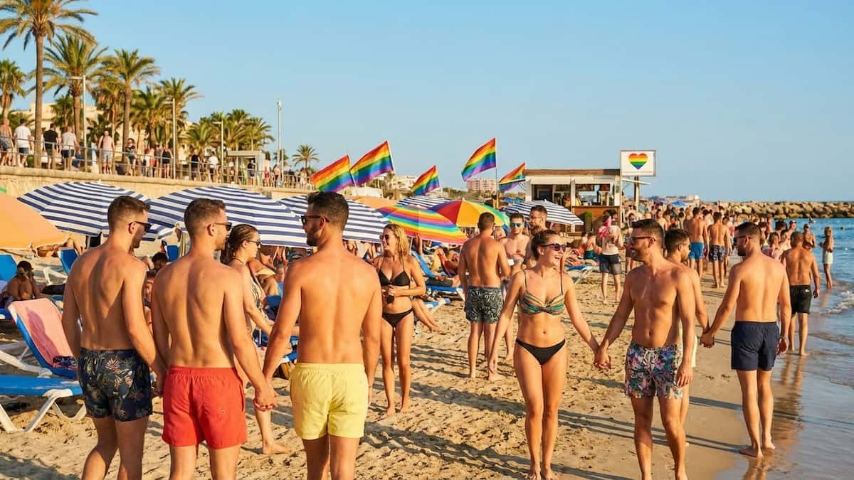 Playa LGBT con banderas arcoíris y parejas disfrutando de un destino de turismo rosa.