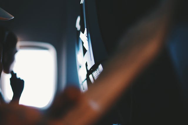Interior de un avión con pantalla de entretenimiento y pasajero junto a la ventanilla