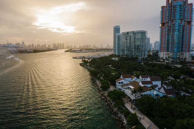 Vista aérea de Miami al atardecer con edificios frente al mar y barcos en la bahía.