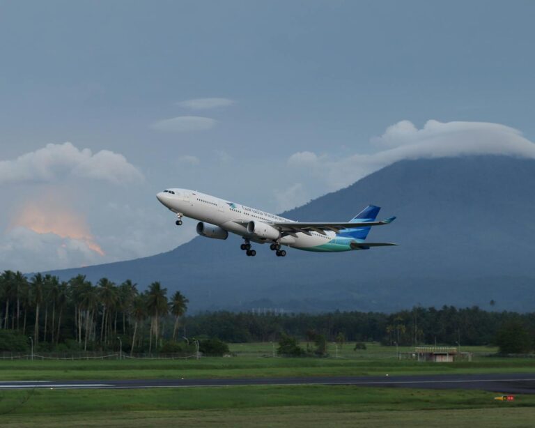 Avión de Garuda Indonesia despegando con montañas al fondo y palmeras en primer plano.