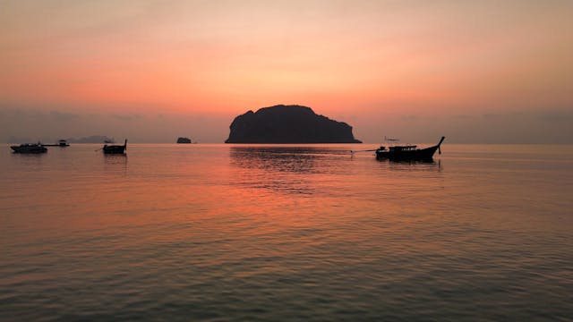 Atardecer sobre el mar en Tailandia con botes tradicionales y una isla al fondo