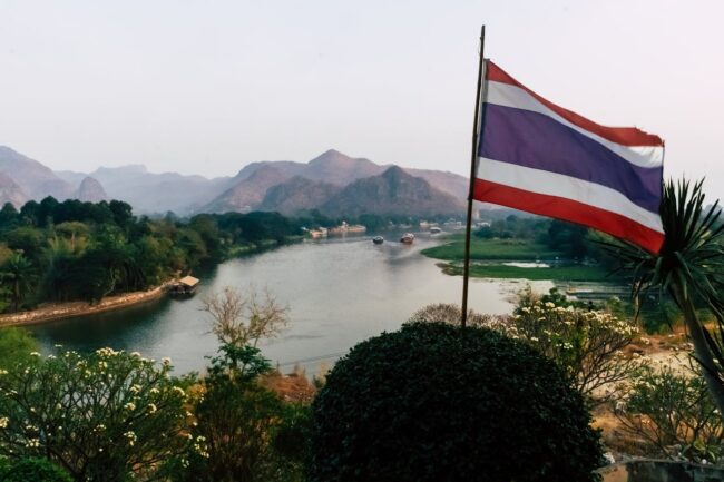 Paisaje natural de Tailandia con r&iacute;o, monta&ntilde;as y bandera tailandesa en primer plano