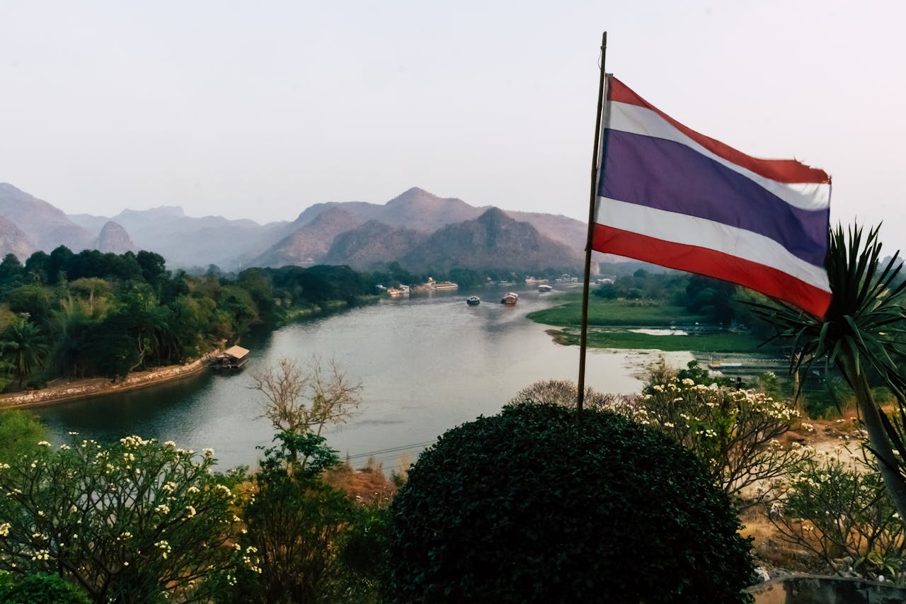 Paisaje natural de Tailandia con río, montañas y bandera tailandesa en primer plano
