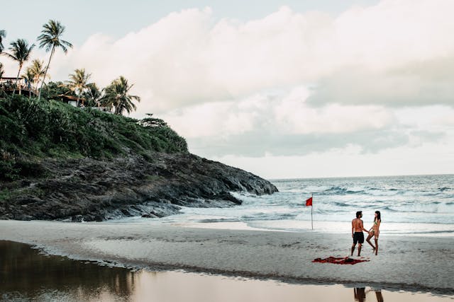 Pareja disfrutando de una playa tropical con bandera roja y fondo rocoso.