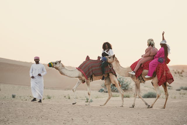 Turistas montando camellos en el desierto de Dubái durante un safari al atardecer
