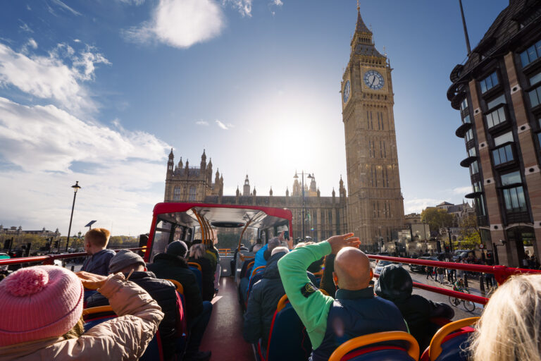 Autobús turístico City Sightseeing London de dos pisos, con diseño colorido, frente al Big Ben en Londres.
