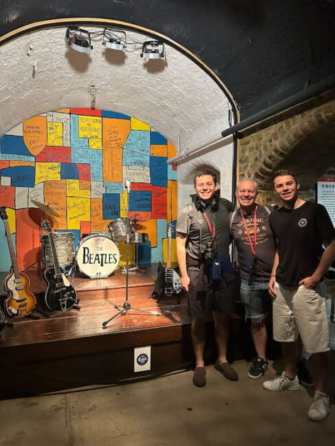 Escenario con instrumentos de The Beatles en Liverpool, junto a visitantes emocionados. Visitantes posando frente al escenario con instrumentos de The Beatles en The Beatles Story, Liverpool.