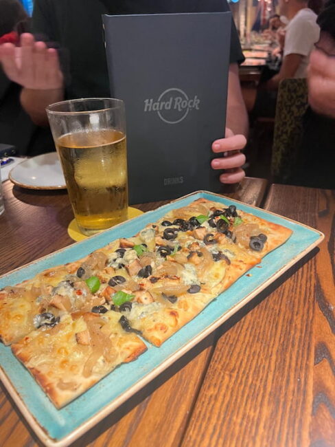 Flatbread con pollo y cerveza en el Hard Rock Cafe London. Flatbread con queso, pollo, cebolla caramelizada, aceitunas negras y pimientos verdes servido con una cerveza en el Hard Rock Cafe de Londres.