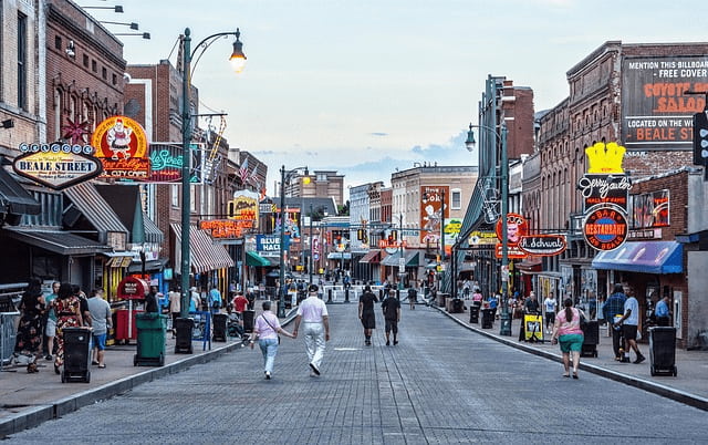 Turistas caminando por la animada Beale Street en Memphis, con carteles de neón y bares icónicos.