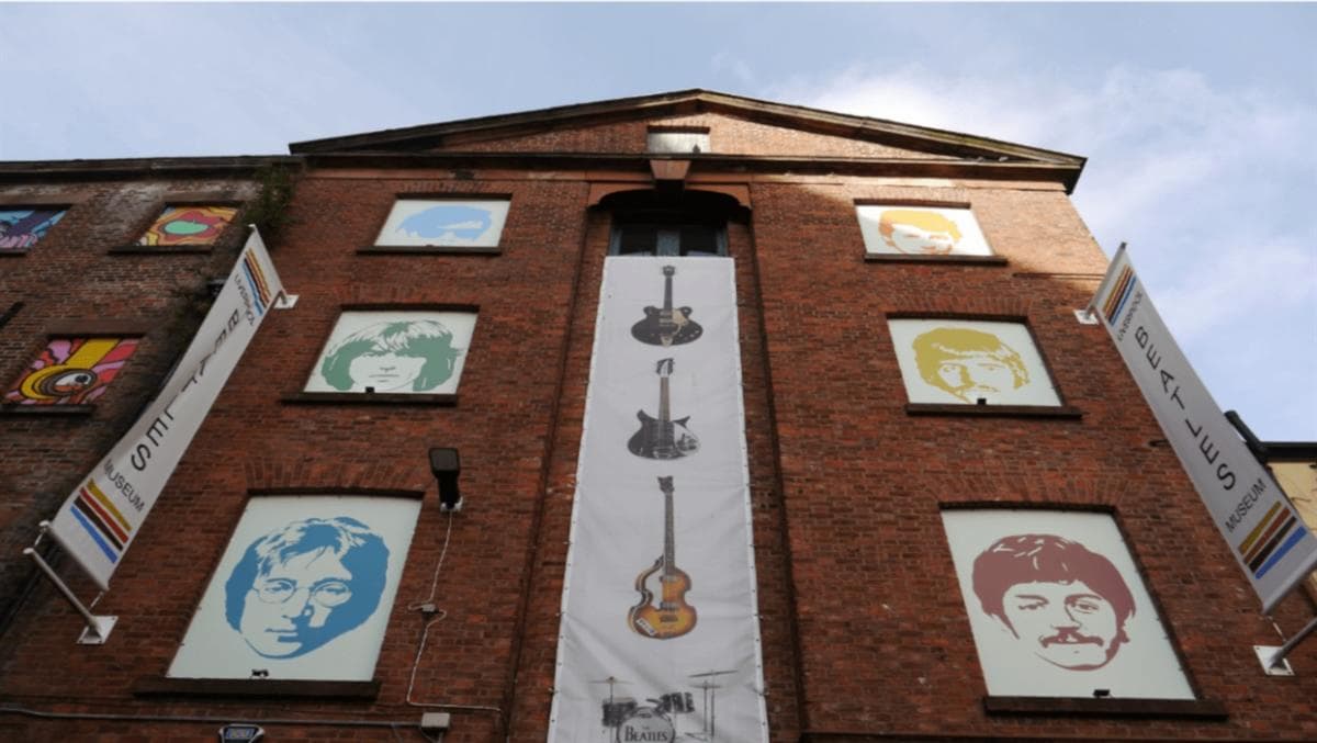 Fachada del Liverpool Beatles Museum con ilustraciones de los cuatro miembros de la banda en colores pop y un cartel vertical con instrumentos musicales.