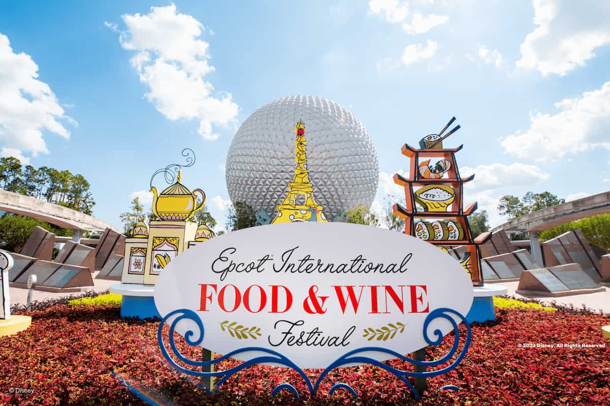 Cartel del EPCOT International Food & Wine Festival frente a la icónica esfera de Spaceship Earth en Walt Disney World, rodeado de decoraciones culinarias de inspiración internacional.