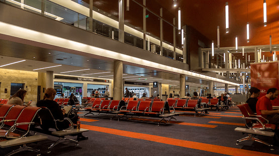 Sala de embarque en el Aeropuerto Ezeiza con asientos rojos, tiendas duty free y pasajeros esperando sus vuelos.