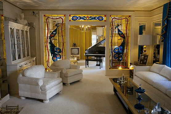Interior elegante de Graceland con sillones blancos, detalles en vitral de pavos reales y un piano de cola negro en la sala principal.