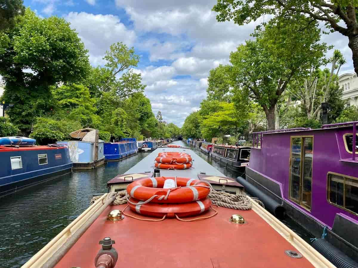 Vista desde un paseo en barco por el canal de Little Venice, con barcos narrowboats a ambos lados y árboles frondosos.