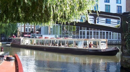 Crucero panorámico por los canales de Londres, una experiencia tranquila y pintoresca. Paseo en barco por los canales de Londres, con turistas a bordo disfrutando del paisaje urbano y natural.