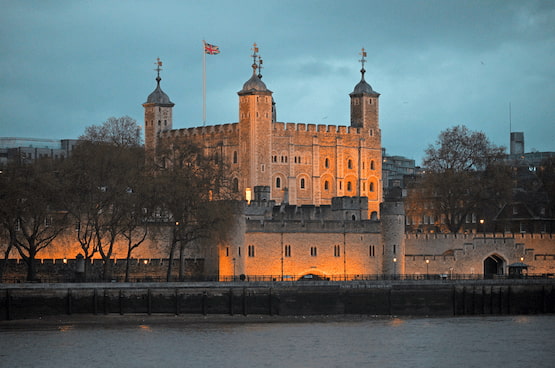 Torre de Londres iluminada durante el atardecer en la ribera del Támesis. Torre de Londres iluminada al atardecer con bandera británica ondeando, vista desde el río Támesis.