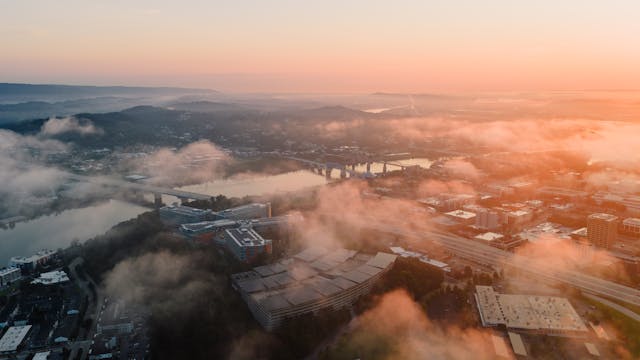 Vista aérea de una ciudad al amanecer con niebla y puentes sobre el río.