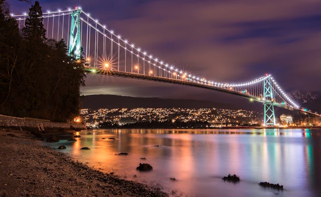 Puente Lions Gate iluminado por la noche con reflejos de luces sobre el agua en Vancouver

