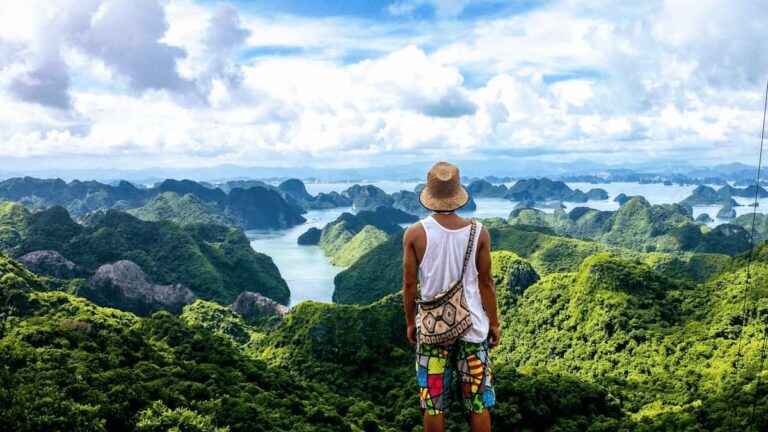 Viajero con sombrero observando una espectacular vista panorámica de islas montañosas cubiertas de vegetación tropical y mar azul.