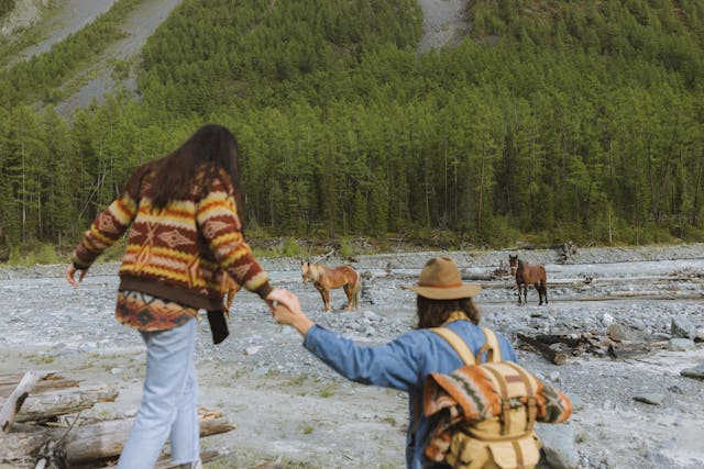 Aventura al aire libre: avistamiento de caballos salvajes en la montaña. Pareja de excursionistas observa caballos salvajes en un paisaje montañoso con bosque.