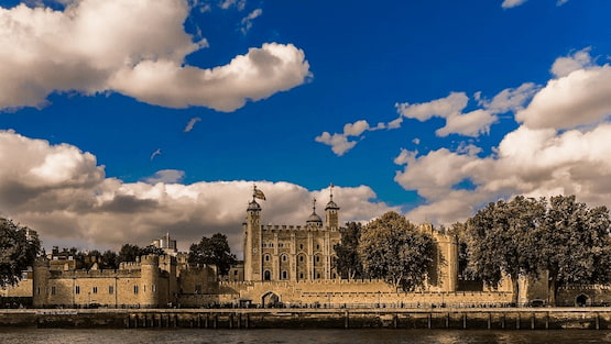 Torre de Londres, un monumento histórico a orillas del Támesis. Vista panorámica de la Torre de Londres con cielo azul y nubes, tomada desde el río Támesis.