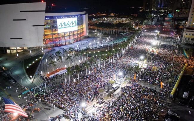 Multitud de corredores participando en la Maratón de Miami frente al estadio bajo luces nocturnas.