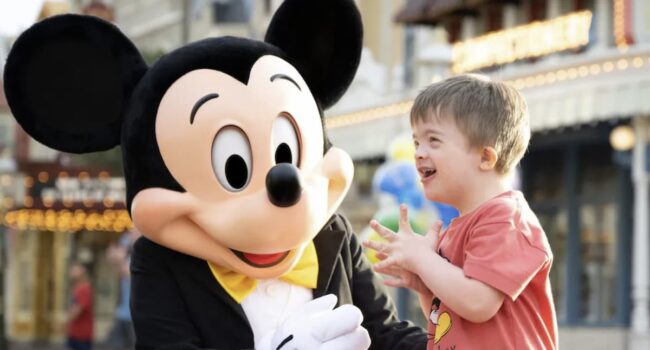 Niño sonriente junto a Mickey Mouse en Disney, disfrutando de una experiencia inclusiva y mágica.